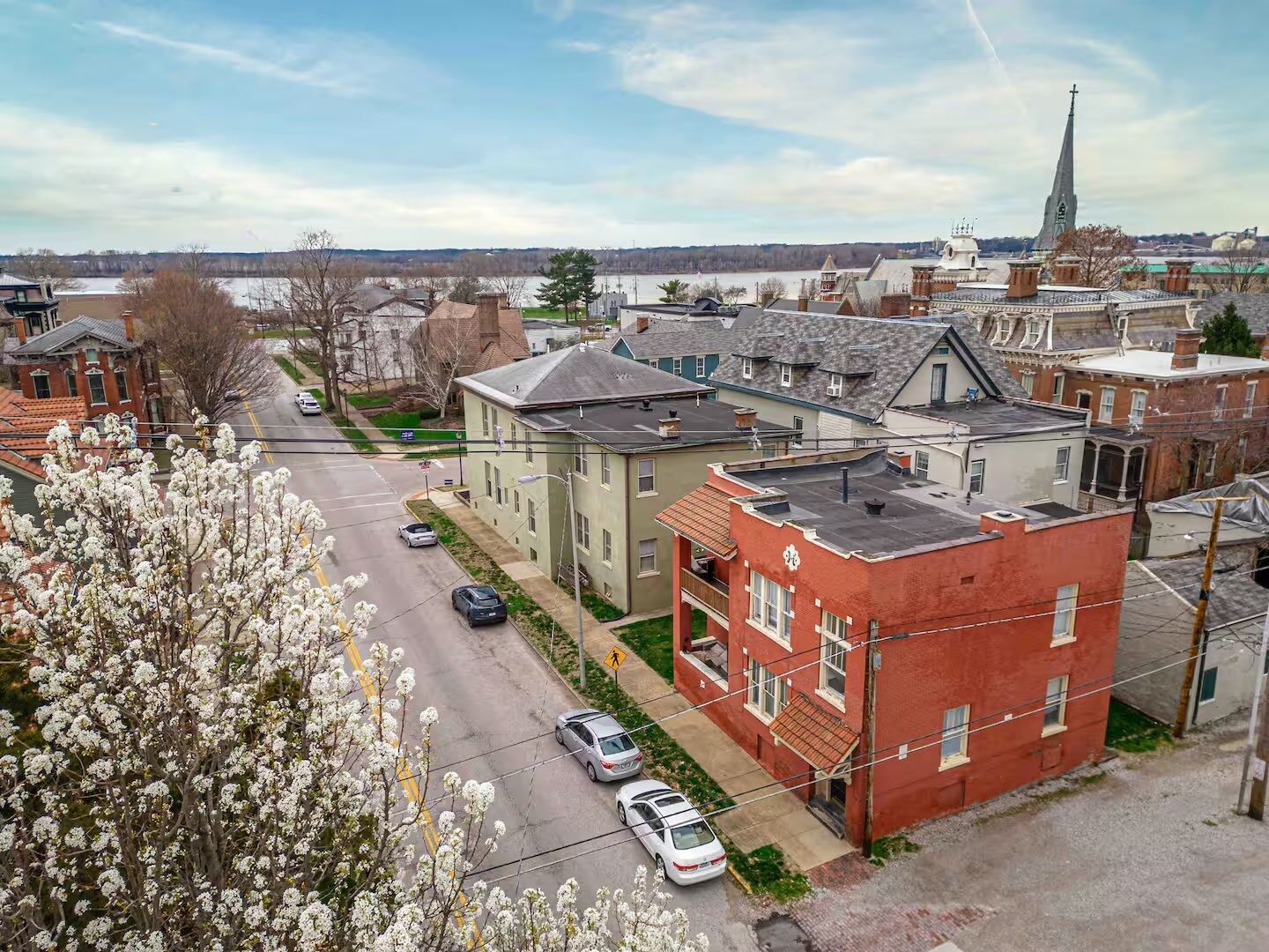 A residential area with a mix of single and multi-story houses, a church with a tall steeple, and a road with parked cars.