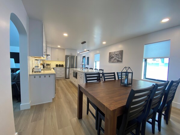 A modern kitchen with white cabinets, a large island, and a dining area with a wooden table and chairs.
