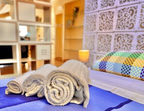 A neatly made bed with rolled towels, a colorful quilt, and a decorative wall panel. - Casuzza Bedda - Appartamento con vista mare (Trappitello)