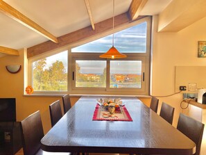 Un comedor con una mesa grande, sillas, una lámpara colgante y vistas amplias por un ventanal.