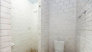 A small, white brick-walled bathroom with a toilet and a shower.