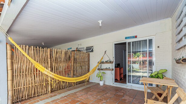 A covered patio area with a bamboo fence, a hammock, a wooden table, and a potted plant.