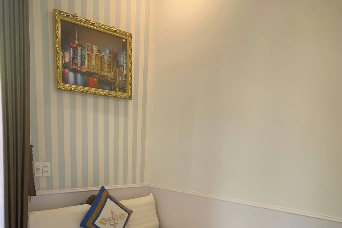 Een opgemaakt bed met een wit-blauwe deken, een lijst met een foto aan de muur en een houten nachtkastje.