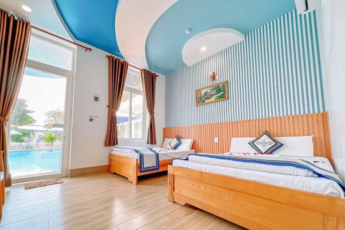 Hotelkamer met twee houten bedden, uitzicht op een zwembad en een plafond met een blauw-wit gestreept patroon.