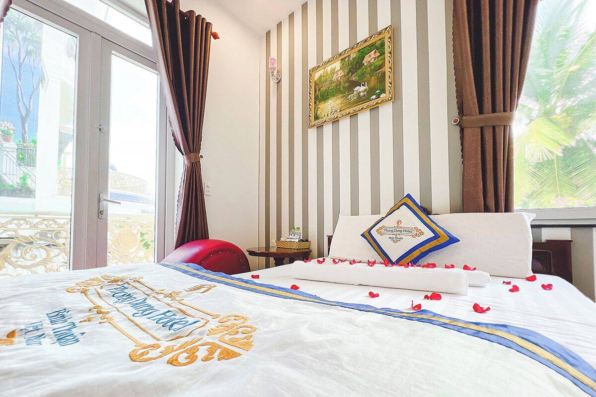 Een hotelkamer met een bed, gordijnen, een schilderij en uitzicht op het omliggende landschap.
