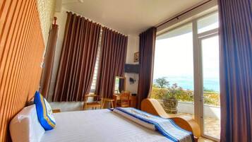 A hotel room with a bed, a desk, a chair, and a balcony with a view.