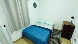 Une petite chambre à coucher, bien rangée, avec un lit, une table de chevet, une lampe et un radiateur.