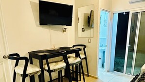 Un coin repas avec une table et des chaises, un téléviseur à écran plat fixé au mur et une porte-fenêtre coulissante donnant sur un espace extérieur.