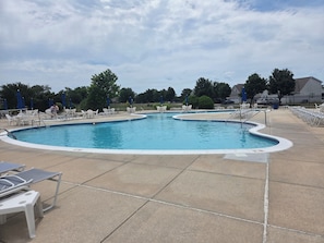 A swimming pool with lounge chairs and umbrellas, surrounded by a fence and trees.