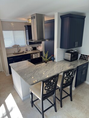 Una cocina moderna con encimeras de granito, muebles oscuros y una isla central con taburetes de bar.