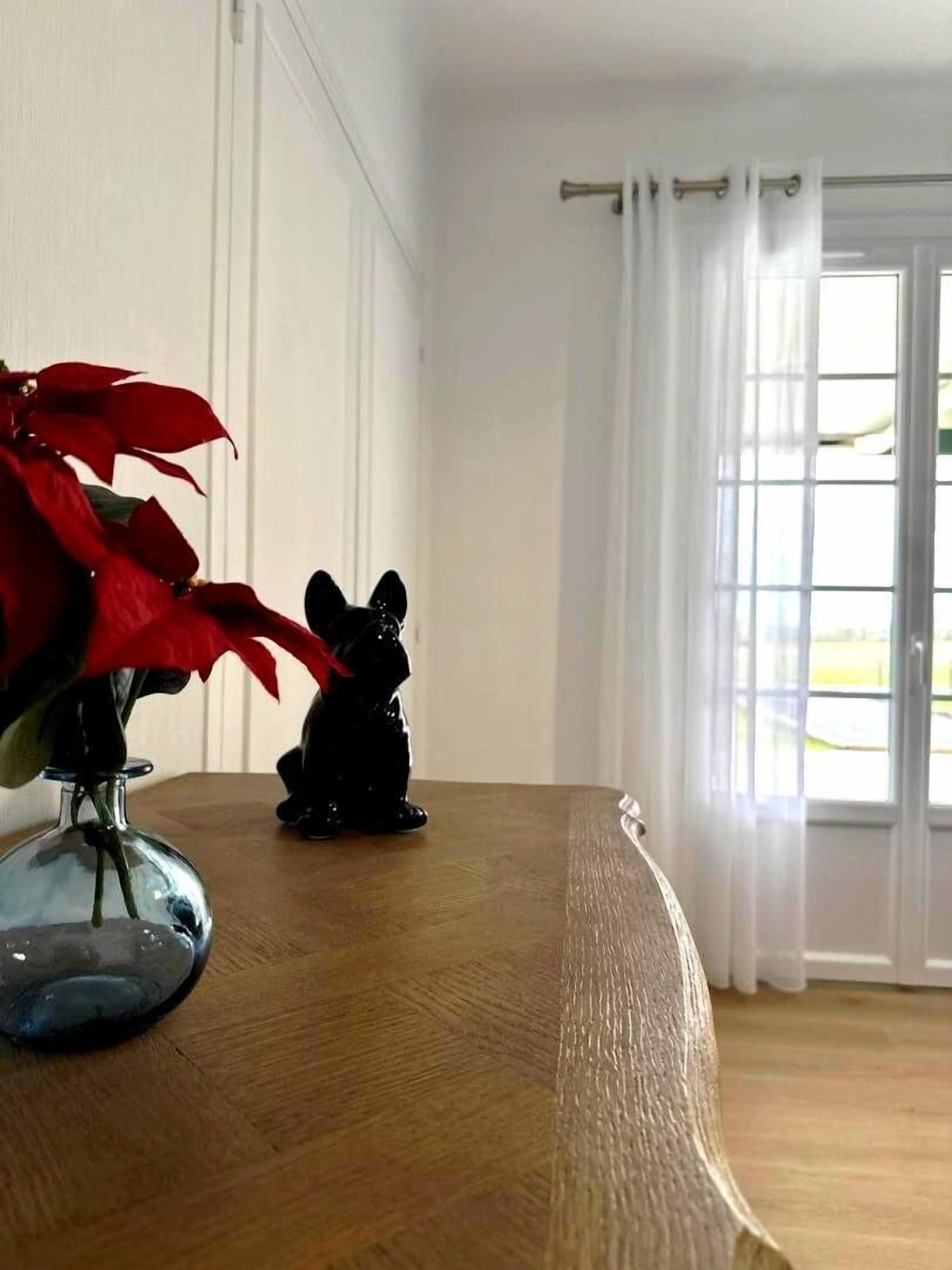 Een kamer met een houten tafel, een vaas met rode bloemen en een kleine beeldje.
