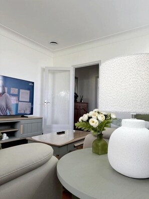 Ein stilvolles Wohnzimmer mit Fernseher, einem runden Tisch, einer Blumenvase und einer großen weißen Lampe.