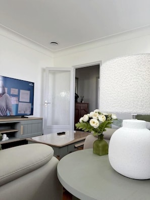 Ein modernes Wohnzimmer mit Fernseher, einem runden Tisch, einer Blumenvase und einer großen weißen Lampe.