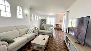Uma sala de estar com sofá, poltronas, mesa de centro e televisão.