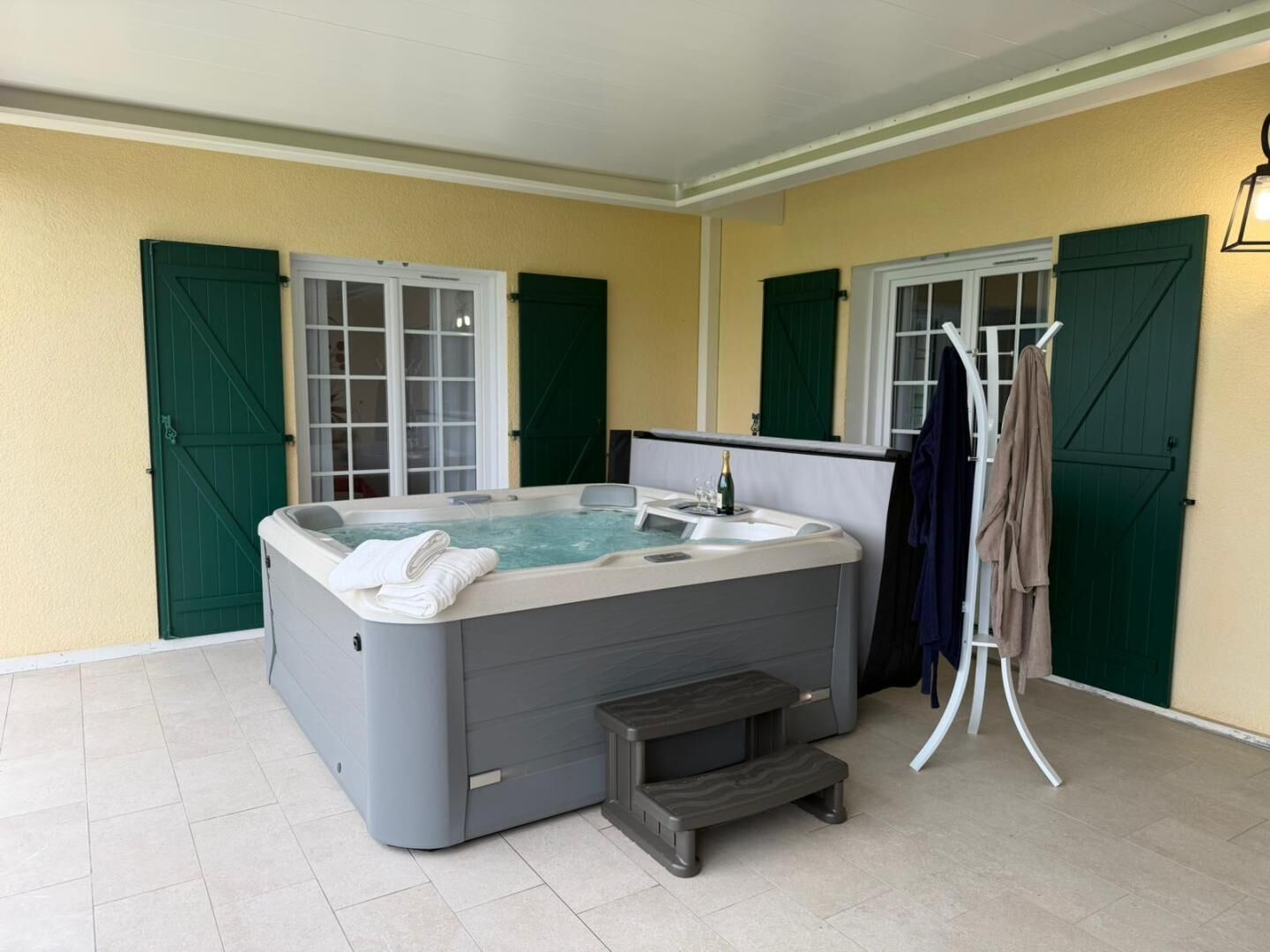 A hot tub in a room with green shutters and tiled flooring.