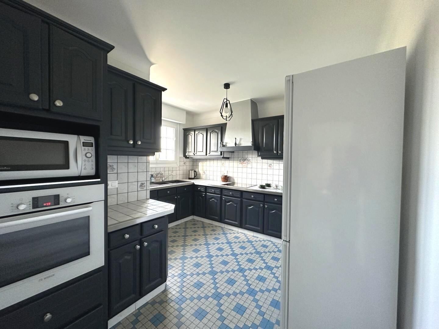 A kitchen with dark cabinets, a white refrigerator, and a blue and white checkered floor.
