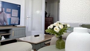 Uma sala de estar moderna com televisão, uma mesa redonda, um vaso com flores e um abajur branco grande.