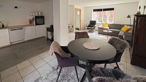 A modern kitchen with a dining area featuring a round table and chairs, a sofa, and a window with a view of buildings. - Lovely home in Rudkøbing with WiFi (Rudkøbing)