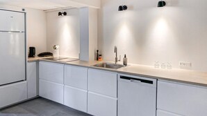A modern kitchen with white cabinetry, a built-in dishwasher, a stainless steel refrigerator, a sink with a faucet, and wall-mounted lighting. - Lovely home in Rudkøbing with WiFi (Rudkøbing)