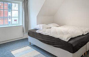A bedroom with a bed, a window with curtains, and a view of buildings outside.
