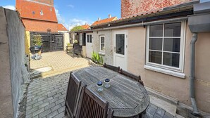 A courtyard with a wooden table and chairs, a grill, and a brick pathway. - Lovely home in Rudkøbing with WiFi (Rudkøbing)