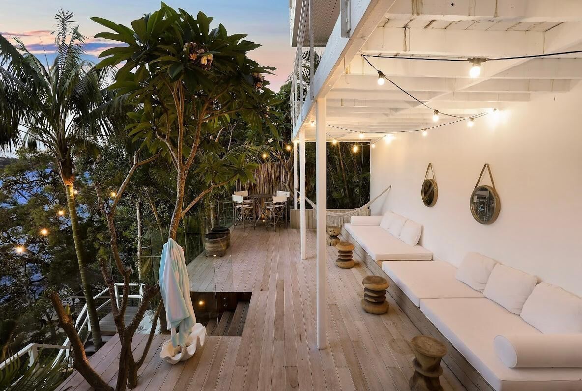 Een moderne buitenlounge met een witte bank, houten tafels en sfeerverlichting.