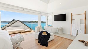 Une pièce moderne et bien éclairée, dotée d’une grande fenêtre offrant une vue panoramique, d’un coin salon confortable et d’un téléviseur à écran plat fixé au mur.