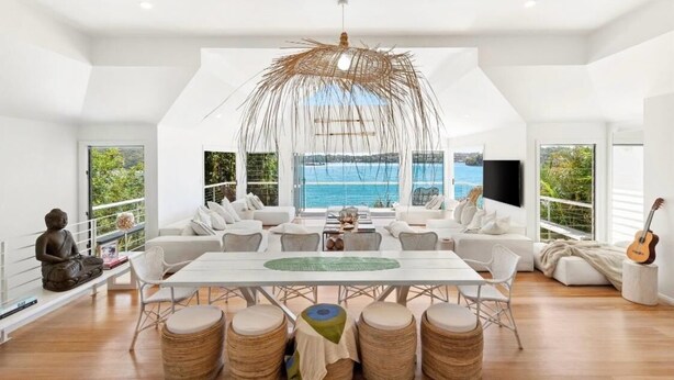 Un vaste espace de vie comprenant une grande table, des canapés blancs et une vue sur la mer.