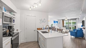 A modern kitchen with a central island, a dining area with blue sofas, and a living room with a large window. - *Heart of Orange Beach - Gulf front*Pool*Balcony (Orange Beach)