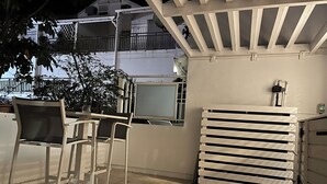Uma área de pátio com móveis de exterior, um radiador branco e vista para um prédio residencial ao fundo.