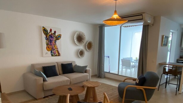 Uma sala de estar moderna com um sofá, duas mesas laterais de madeira, uma cadeira e uma grande janela com vista.