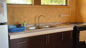 A kitchen with wooden cabinets, a stainless steel sink, a clock, and a window overlooking greenery. - Cabaña El Tilo - Getaway with a view of Ranco Lake (Riñinahue)
