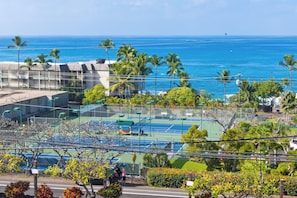 Una cancha de tenis con vista al océano y palmeras.