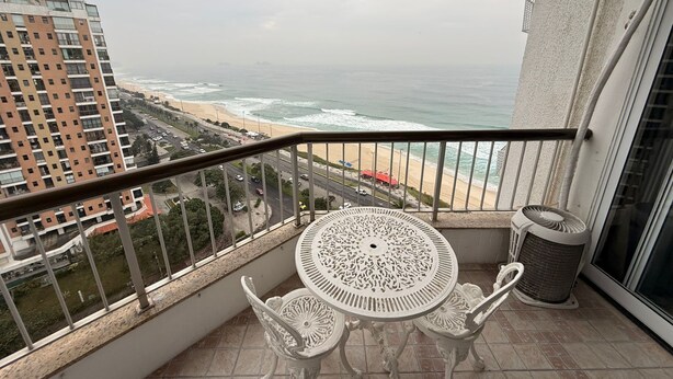 A balcony with a table and chairs, overlooking a beach and ocean. - Beach dream, sea and lagoon views, fully equipped apartment. (Rio de Janeiro)