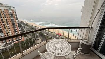 A balcony with a table and chairs, overlooking a beach and ocean.