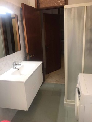 A bathroom with a white sink, a mirror, a shower, and a toilet. - Holiday apartment mit Klimaanlage und Balkon (Lido di Jesolo)