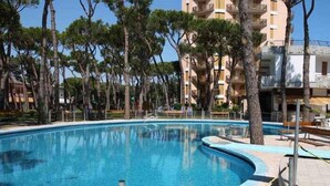 Una piscina de borde curvo, rodeada de árboles y un edificio con balcones.