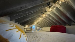 An attic bedroom with a sloped ceiling, exposed wooden beams, and string lights.