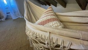A hammock with macrame fringe, a patterned pillow, and a view of a window with sheer curtains.
