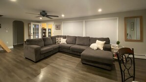 A living room with a sectional sofa, a ceiling fan, and a dining area with a chair and table.