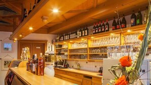 A bar area with shelves of wine bottles and glasses, a wooden counter, and a decorative flower arrangement. - Hotel Restaurant Piccolo (Thale)