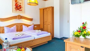 A hotel room with a bed, a television, a wooden cabinet, a table with fruit, and a painting on the wall. - Hotel Restaurant Piccolo (Thale)