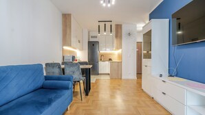 A modern living room with a blue sofa, a dining area, and a kitchen with white cabinets and a built-in oven. - Szybowcowa Charming Apartment (Katowice)