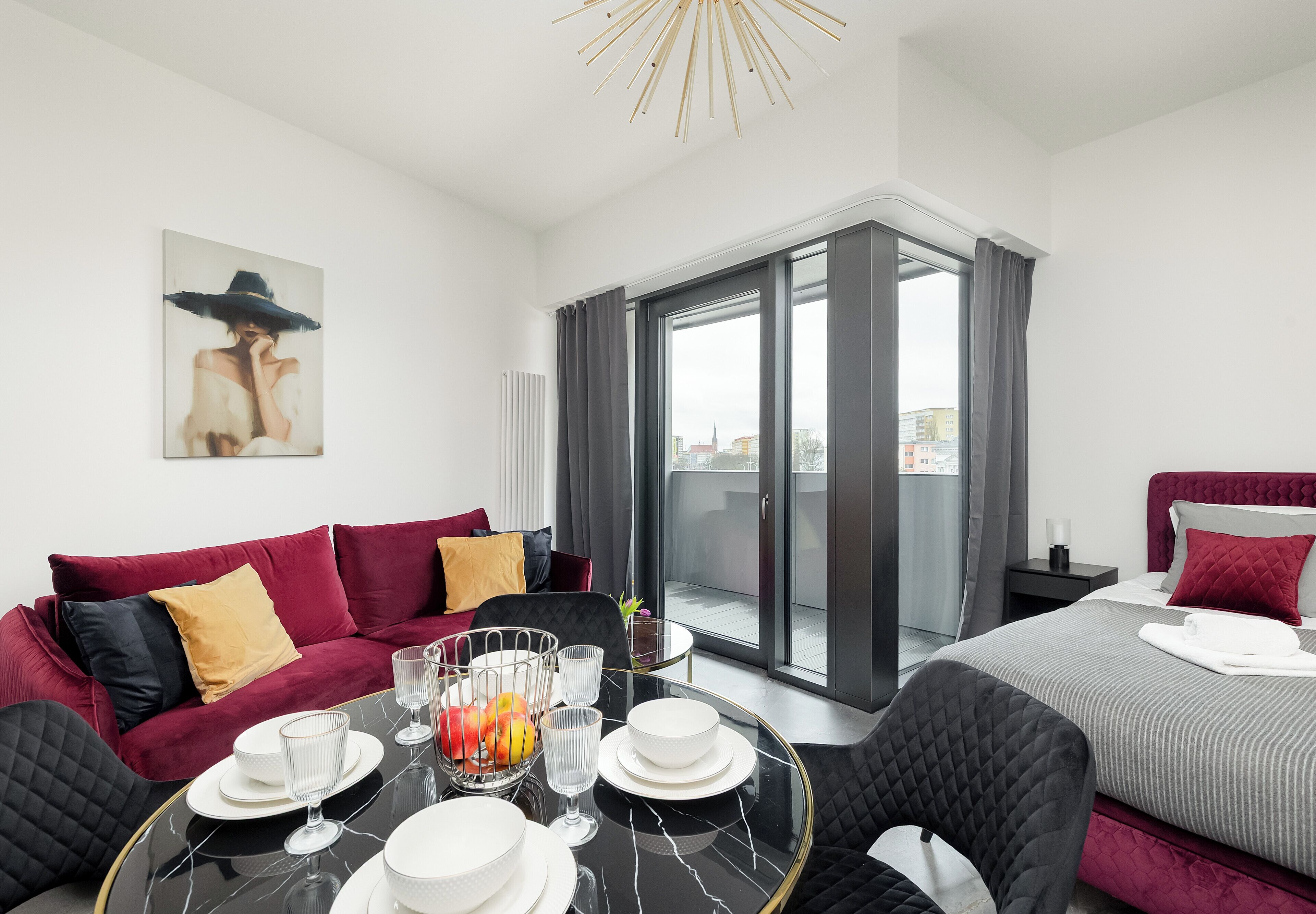 A modern hotel room with a balcony, a dining table set with white plates and glasses, and a large window with curtains.