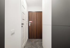 A hallway with a wooden door, a white wall, and a grey floor. - Hanza Tower Studio 309 (Szczecin)