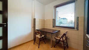A small, clean room with a dining table and two chairs, a window with blinds, and a door with a handle. - Hłaski Urban Cozy Apartment (Wrocław)