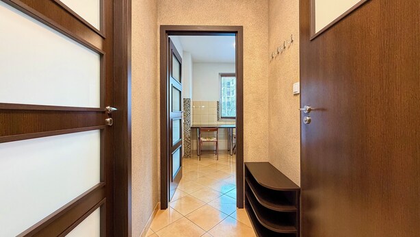 A hallway with wooden doors, a tiled floor, and a view into a room with a dining table and chairs. - Hłaski Urban Cozy Apartment (Wrocław)
