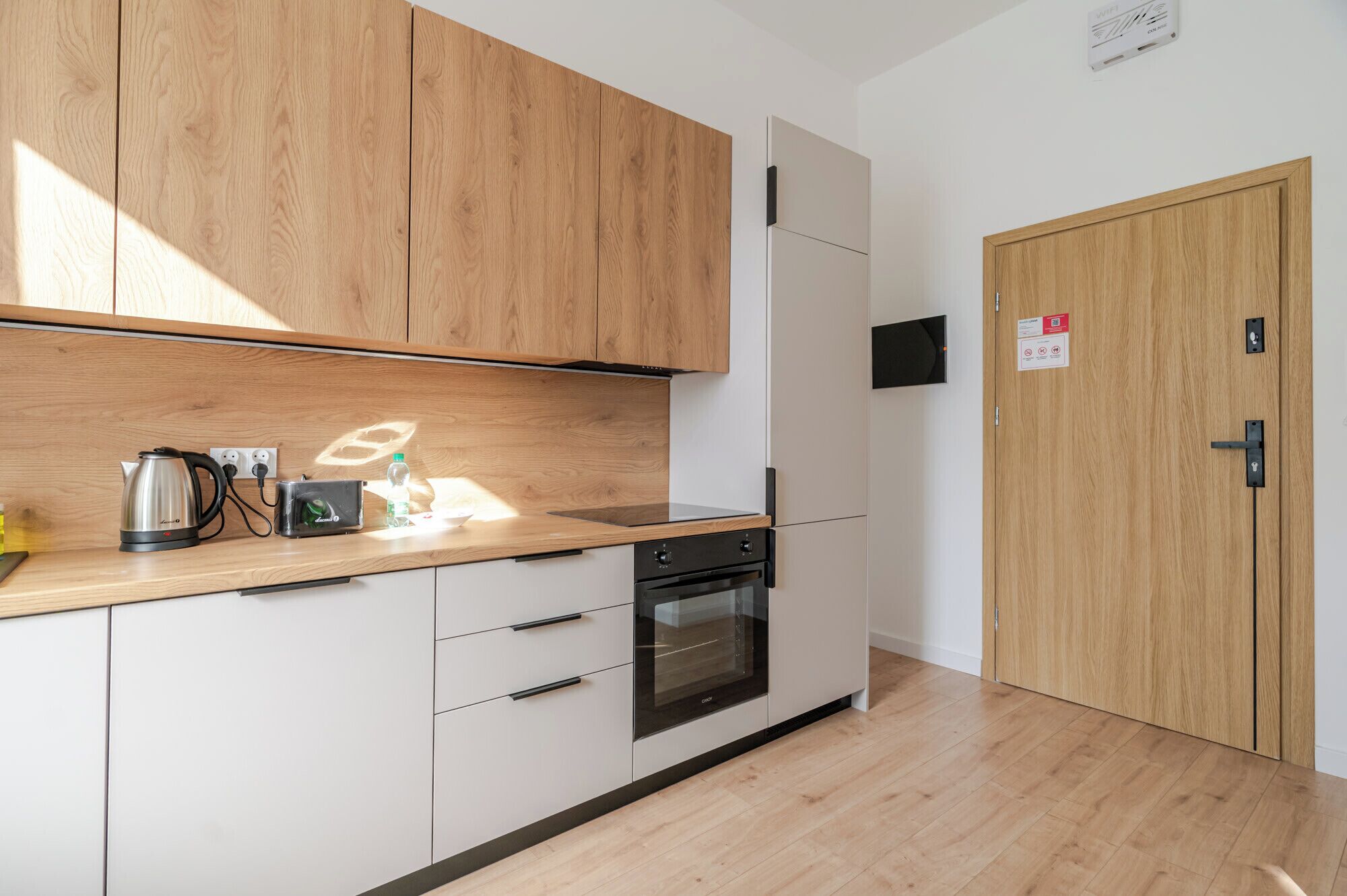 Eine moderne Küche mit Holzausstattung, einem eingebauten Backofen und einer Arbeitsfläche mit Wasserkocher und Wasserflasche.