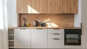 Una cocina moderna con armarios de madera, un lavamanos de acero inoxidable, una tetera, un recipiente para hervir agua y un horno.