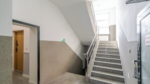 Una escalera que sube a un piso superior, una puerta con un cartel verde y una pared con textura.